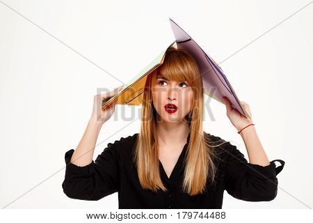 Young successful businesswoman holding folders above head, thinking over white background. Copy space.