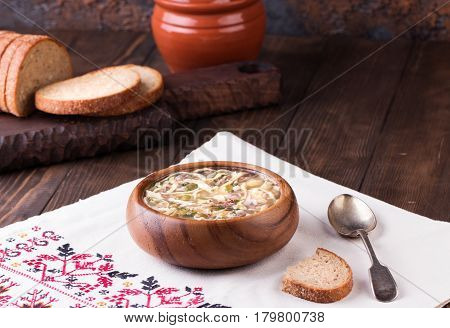 Traditional russian Cold Soup Okroshka with meat, vegetables and kvass serving size in wooden bowl and rye bread on wooden table. Kvass is a traditional Slavic and Baltic fermented beverage commonly made from rye bread