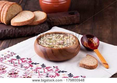 Traditional russian Cold Soup Okroshka with meat, vegetables and kvass serving size in wooden bowl and rye bread on wooden table. Kvass is a traditional Slavic and Baltic fermented beverage commonly made from rye bread