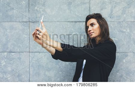 Portrait young businesswomen in black suit using smartphone isolated on background concrete gray wall mockup pretty hipster manager holding mobile gadget girl making selfie photo connect