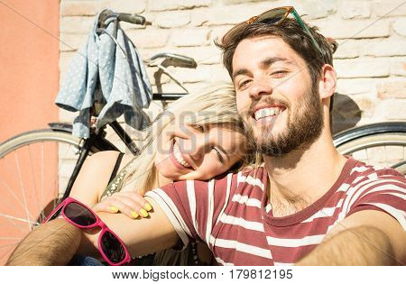 Happy hipster couple taking selfie at old town trip with vintage bicycle - Fun concept with alternative fashion city travelers - Handsome boyfriend with caucasian girlfriend - Warm bright vivid filter