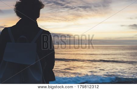 Young hipster relax on the beach on background ocean sunrise silhouette romantic person looking view evening seascape girl enjoy sunset on coast travel holidays vacation back figure on backdrop sea