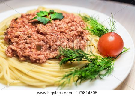 hot spaghetti with red meat sauce , cherry tomoto and parsley on big white plate on a wood table . Health food concept