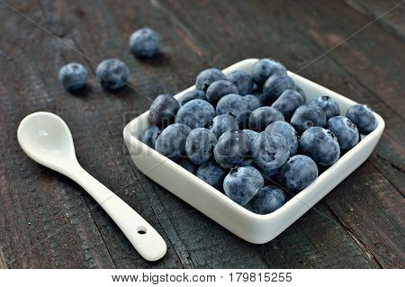 Blueberry fruit on wood background. Forest fruit in white idaeus and spoon. Delicious fresh berries.