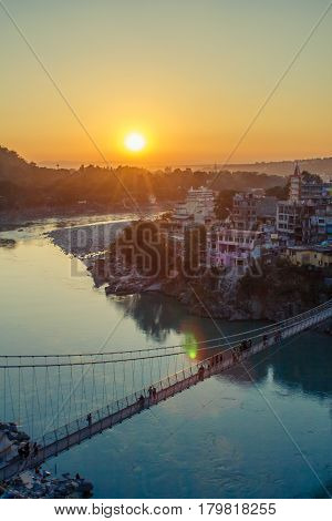 View of River Ganga and Lakshman Jhula bridge at sunset with a blue sky and colorful houses. Rishikesh. India. HDR image
