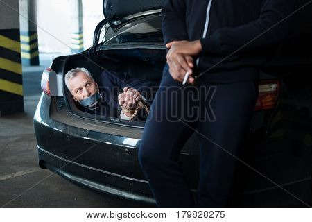 Successful assault. Nice calm adult man holding a cigarette and smoking it while enjoying leaning on the car boot