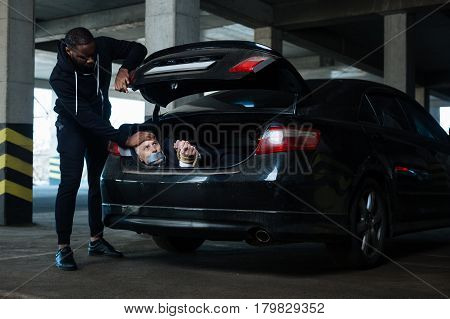 Victim of kidnapping. Frightened unhappy elderly man being in the car boot and looking at his kidnapper while having his hands tied
