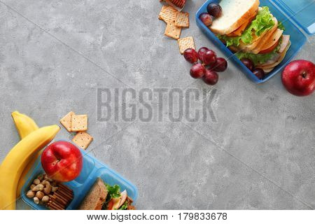 Lunchboxes with sandwiches and different products on grey background