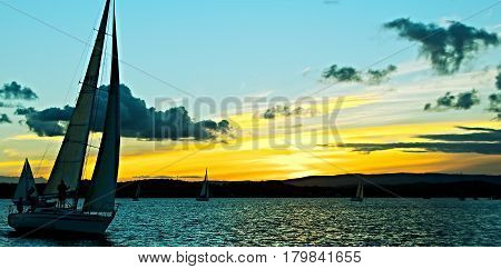 Sailing yacht in silhouette with golden sunset and water reflections. Photo captured in Lake Macquarie New South Wales Australia.