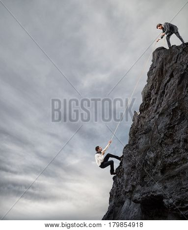 Businessman helps another man to climb a mountain. Businessmen collaborate to achieve a goal concept.