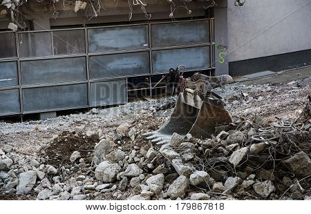 Excavator shovel lies in the rubbish of a demolished building dirty and gray contruction site in the inner city urban scene