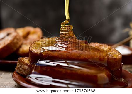 honey dropping on some torrijas, typical spanish dessert for Lent and Easter, served in an earthenware plate, on a rustic wooden table