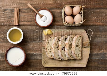 high-angle shot of a rustic wooden table with the ingredients to prepare spanish torrijas, typical sweet food eaten in Lent and Easter, such as bread, eggs, cinnamon, milk, sugar or olive oil