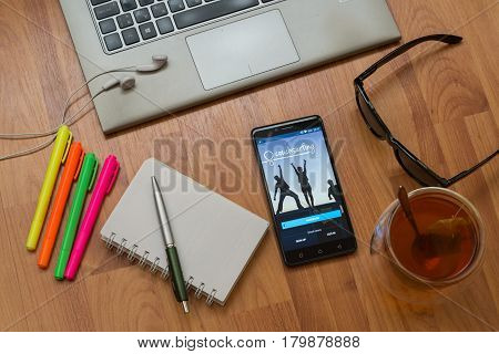 Nitra, Slovakia, april 3, 2017: Couchsurfing application in a mobile phone screen. Workplace with a laptop, an earphones, notepad, pen, tea, sunglasses and color markers on wooden background