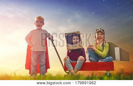 Children in astronaut, pilot and super hero costumes are playing and dreaming. Portrait of funny kids on nature. Family friends games outdoors.