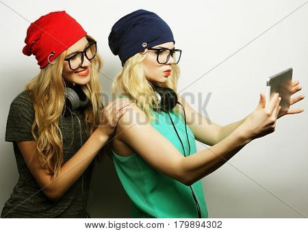 two hipster girls friends taking selfie with digital tablet, studio shot over gray vackground