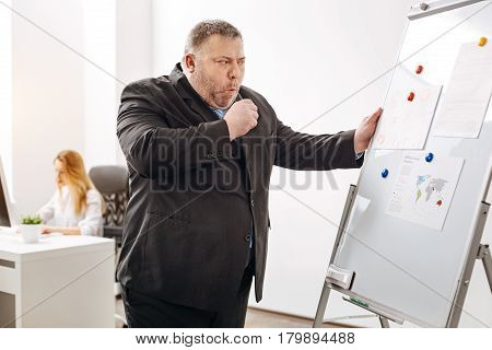 Still doing my job. Engaged chubby middle aged worker standing at the pin board working on the report while being ill