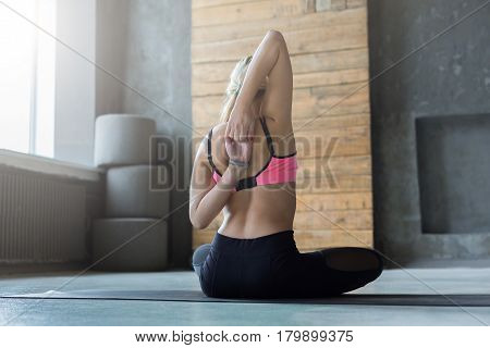 Woman sits and stretch hands behind back at yoga class, gomukhasana exercise. Rear view of flexible yogi girl practicing yoga or pilates, sitting in cow face pose in fitness studio