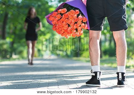 Man hiding bunch of red roses behind his back to surprise his girlfriend