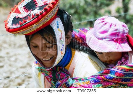 Close up of portrait of a smiling Quechua woman dressed in colourful traditional handmade outfit and carrying her baby in a sling. October 21 2012 - Patachancha Cuzco Peru
