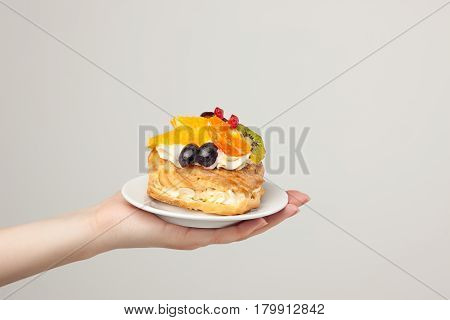 Closeup female hand and cake with fresh fruits isolated on gray background.