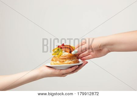 Closeup female hands and cake with fresh fruits isolated on gray background.
