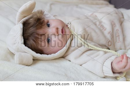 Little Beautiful Baby In A Funny Costume With Ears Lying On His Back.