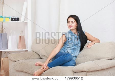 Relaxed casual brunette in blue cardigan and In blue jeans sits on the couch in bright living room