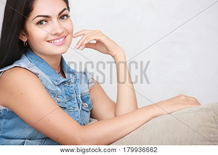 Relaxed casual brunette in blue cardigan and In blue jeans sits on the couch in bright living room
