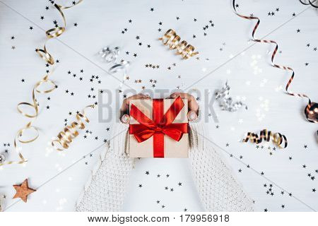 Female hands withbeautiful manicure holding present with red bow on white rustic sparkling background. Festive backdrop for holidays: Birthday, Valentines day, Christmas, New Year. Flat lay style