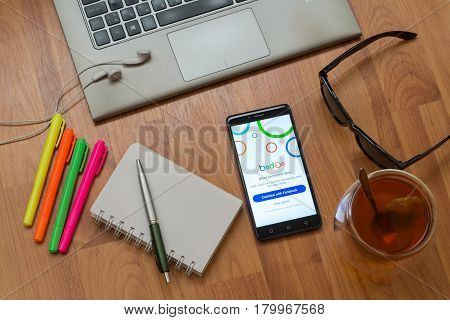 Nitra, Slovakia, april 3, 2017: Badoo application in a mobile phone screen. Workplace with a laptop, an earphones, notepad, pen, tea, sunglasses and color markers on wooden background