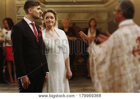 Emotional couple during wedding ceremony handsome happy groom and beautiful bride tearing up during priests speech at wedding ceremony in christian church