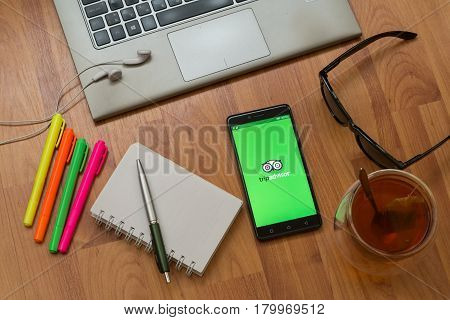 Nitra, Slovakia, april 3, 2017: Tripadvisor application in a mobile phone screen. Workplace with a laptop, an earphones, notepad, pen, tea, sunglasses and color markers on wooden background