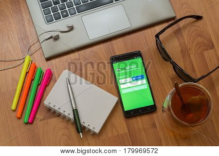 Nitra, Slovakia, april 3, 2017: Tripadvisor application in a mobile phone screen. Workplace with a laptop, an earphones, notepad, pen, tea, sunglasses and color markers on wooden background