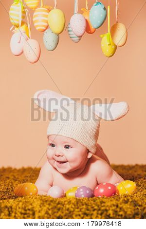 Three months baby lying on his stomach as a Easter bunny on the grass with eggs