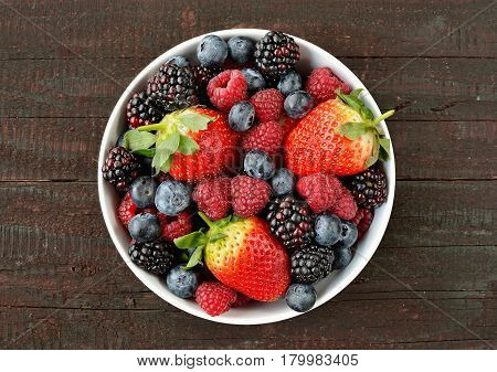 Mix of strawberries, blueberries, blackberries and raspberries fruit on wood table. Forest fruit in white idaeus. Delicious fresh berries.