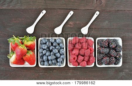 Mix of strawberries, blueberries, blackberries and raspberries fruit on wood table. Forest fruit in white idaeus with spoons. Delicious fresh berries.