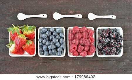 Mix of strawberries, blueberries, blackberries and raspberries fruit on wood table. Forest fruit in white idaeus with spoons. Delicious fresh berries.