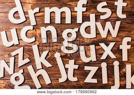 Big letters of the alphabet are chaotically scattered on wooden background. Concept of education