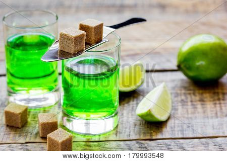 absinthe shots with fresh green lime slices and sugar cubes on wooden bar table background