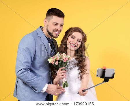 Happy wedding couple making selfie on color background