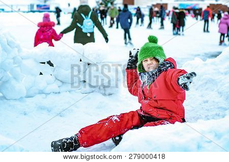 An Angry Funny Boy Throws Snowballs And Builds A Snow Fort Near The City Skating Rink. Winter Activi