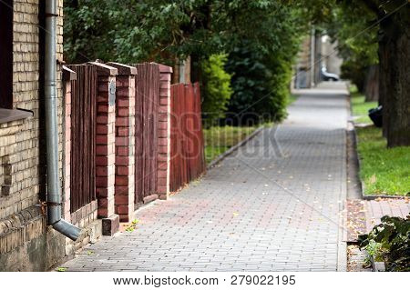 Typical European Summer Cityscape Of Old Street With Paving Slabs, Brick-walled House, Gate And Alle