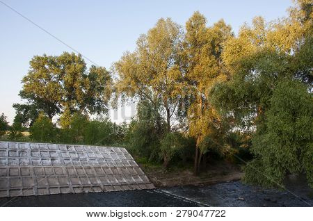 Small River Slow Flowing Across The Green Forest With Reflections Of  Trees In The Water.  Summer