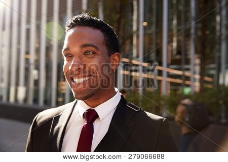Young black businessman wearing black suit standing on the street smiling, close up with lens flare