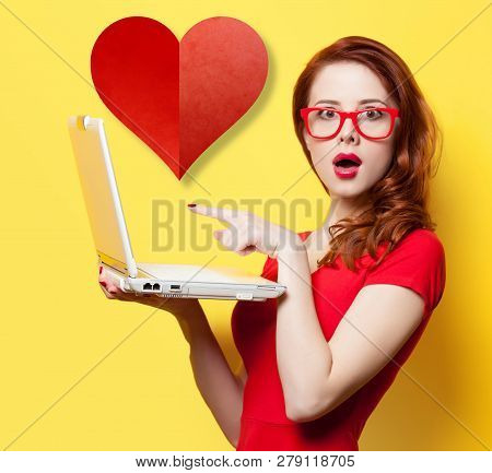 Surprised Redhead Girl With Laptop And Abstract Heart Shape On Yellow Background. In Love Concept Of