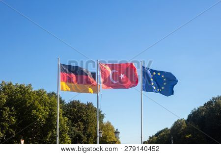 German, European Union, Turkey waving flags on white poles. Looking for co-operation about immigration. Nature and blue sky background.