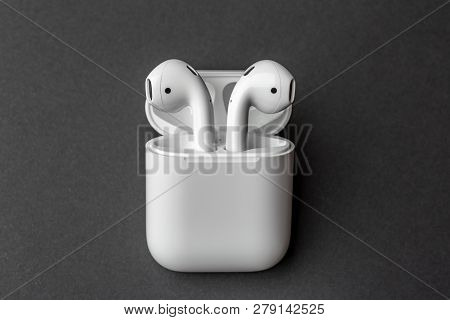 White Wireless Bluetooth Earphones Or Headphones And White Box For Storage And Charging On Dark Grey