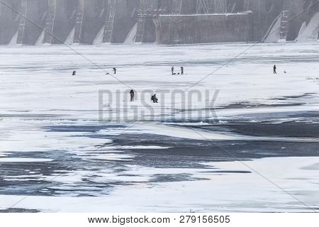 Men In Snow Winter Are Engaged In A Hobby In The Fresh Air. Ice Fish Fishing On The Wide Frozen Rive