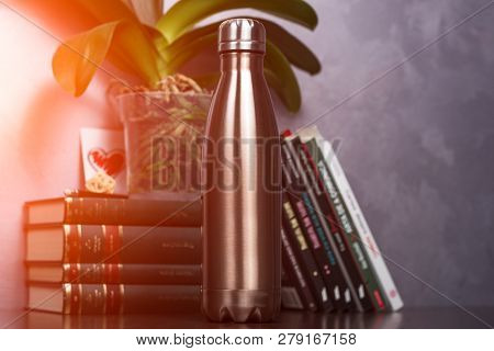 Maro Of Color Thermo Bottle Over Background Of Books And Green Flower. With Sunlight Effect.